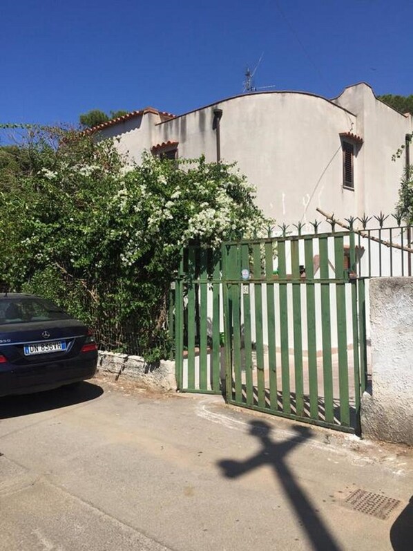 Une entrée fermée par un portail mène à un immeuble, et une voiture est garée à proximité.