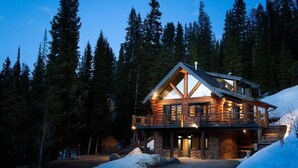 A log cabin with a balcony, surrounded by tall pine trees and snow.
