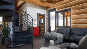 A modern log cabin interior with a staircase, a living area with a sofa and coffee table, and a red cabinet.