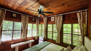 Un dormitorio de cabaña de madera con cama, un banco y un ventilador de techo.