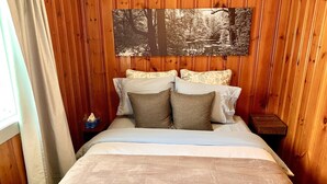 A wooden-paneled room with a bed, pillows, a nightstand, and a wall-mounted picture.
