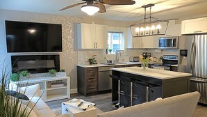 A modern kitchen with a flat-screen TV, a ceiling fan, and a bar area.