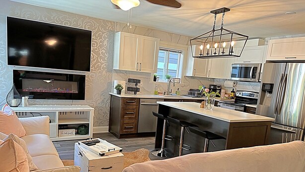 A modern kitchen with a bar area, white cabinetry, and a flat-screen TV.