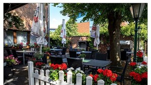 An outdoor patio with tables and chairs, surrounded by a white picket fence and potted plants. - Zum kleinen Reichstag (Moers)