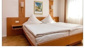 A hotel room with a wooden bed, a nightstand, a wall-mounted lamp, and a framed picture on the wall. - Zum kleinen Reichstag (Moers)