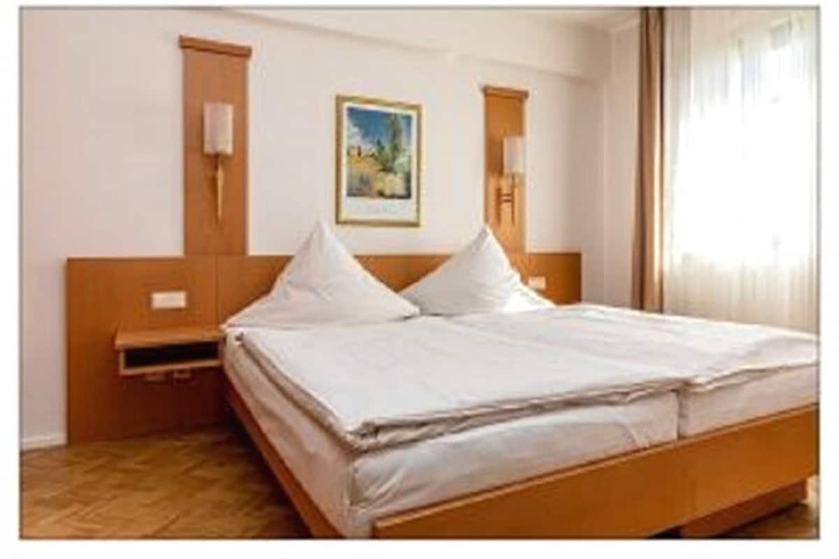 Ein Hotelzimmer mit einem hölzernen Bett, einem Nachttisch, einer Wandlampe und einem gerahmten Bild an der Wand.