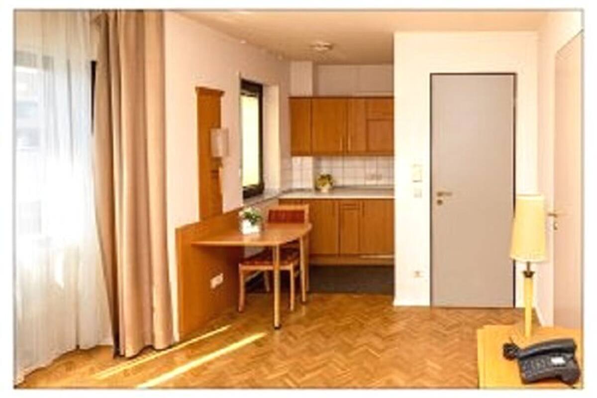 Ein kompaktes Hotelzimmer mit Holzboden, einer Essecke mit Tisch und Stühlen, einer Küchenzeile und einer Tür.