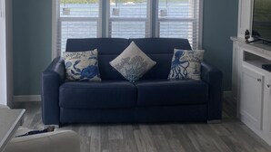 Ein Zimmer mit einem dunkelblauen Sofa, einem großen Erkerfenster und Blick auf das Wasser.
