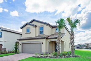 A two-story house with a beige exterior, a garage, and a well-maintained lawn with palm trees. - Luxury and Style! BIG Pool Area and Game Room in Solterra 6br/4.5 Bath #7st564 (Davenport)