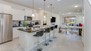 A modern kitchen with white cabinets, stainless steel appliances, and a central island with bar stools. - Luxury and Style! BIG Pool Area and Game Room in Solterra 6br/4.5 Bath #7st564 (Davenport)