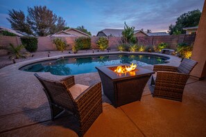 A swimming pool with a fire pit and wicker chairs.
