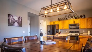 A spacious dining area with a long wooden table and leather chairs, a kitchen with wooden cabinets and a microwave, and a hanging light fixture above. - Goodyear, AZ full home with heated pool and spa and desert oasis back yard!! (Goodyear)
