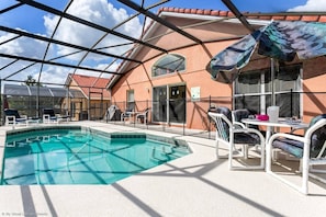 Et poolområde med et klart blåt pool, liggestole og en overdækket terrasse med et bord og stole.