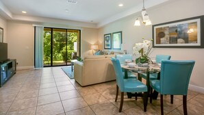A spacious living room with a sofa, a dining table with chairs, and a TV. - Championsgate Town Home Near Top Golf Courses and Disney - 3bd/2.5 Bath #3213 (Davenport)