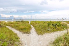 A sandy path leading to a beach with grassy areas and a boat in the distance.