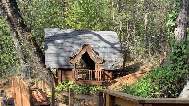 Eine Holzterrasse führt zu einer rustikalen Holzhütte mit Balkon, umgeben von Bäumen.
