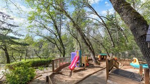Ein Spielplatz mit Rutsche, Spielgeräten und einer Holzterrasse.