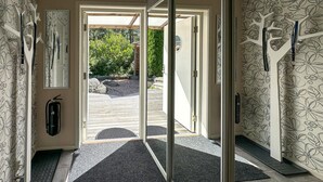 Une entrée moderne avec une porte vitrée donnant sur une terrasse en bois, un extincteur et un paillasson.