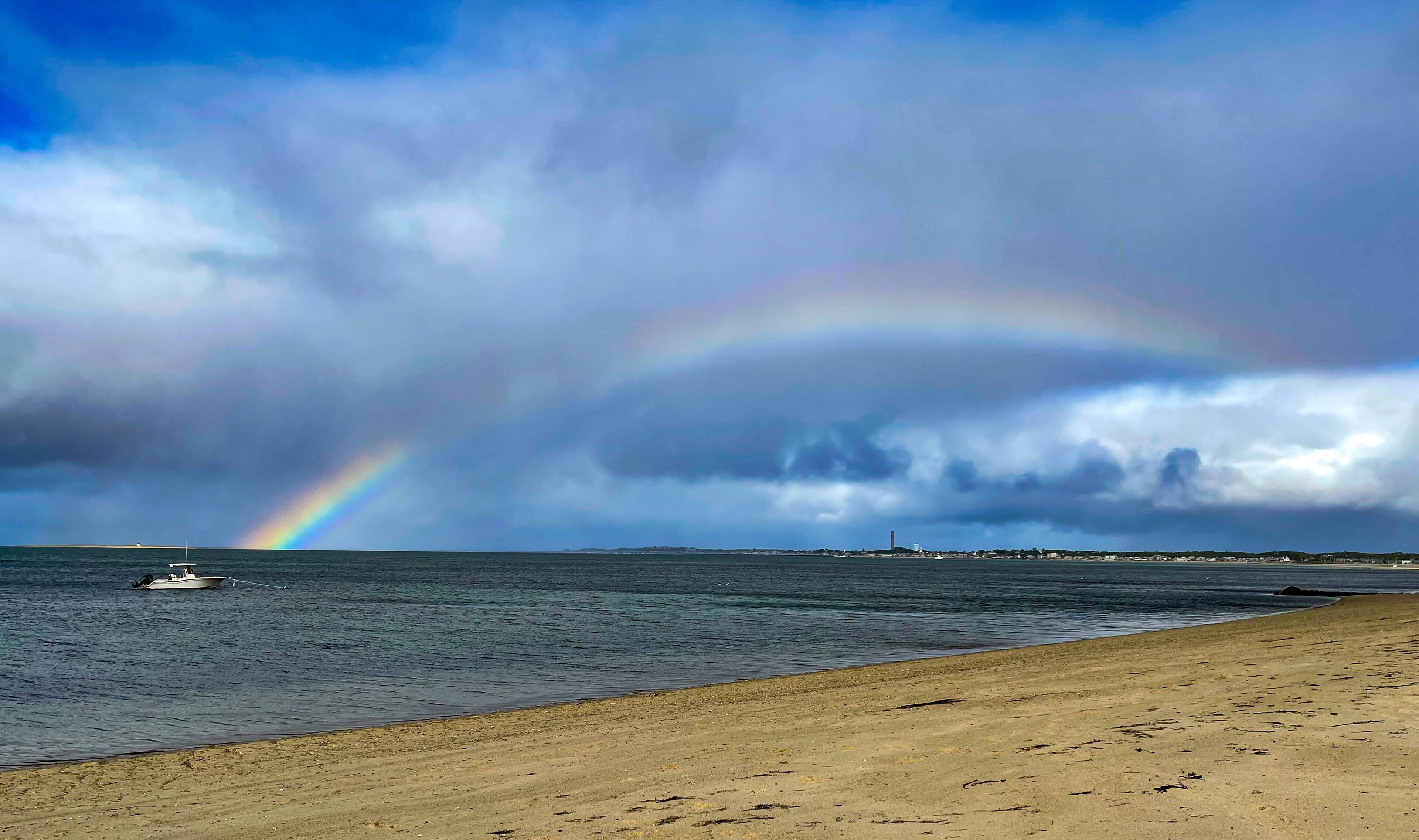 Uma praia com um barco, um arco-íris e um céu nublado.