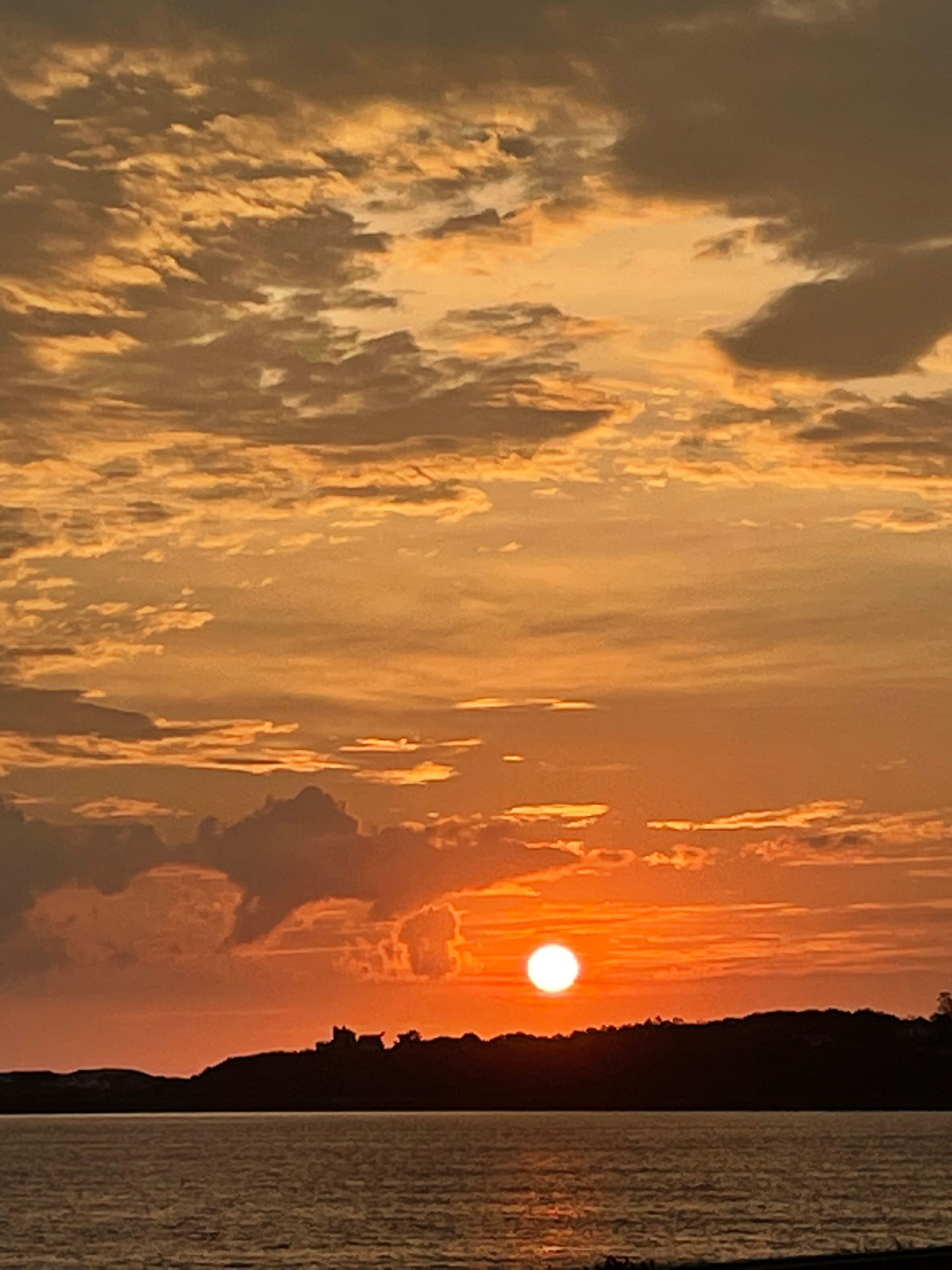 Un atardecer sobre un cuerpo de agua con el silueta de una tierra lejana.
