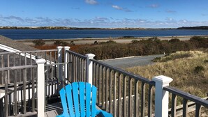 A wooden staircase with a blue chair, leading to a view of a body of water and distant land. - Lovely Oceanview 2 Bed 2 Bath with sleeper sofa, outdoor shower & rooftop deck! (North Truro)