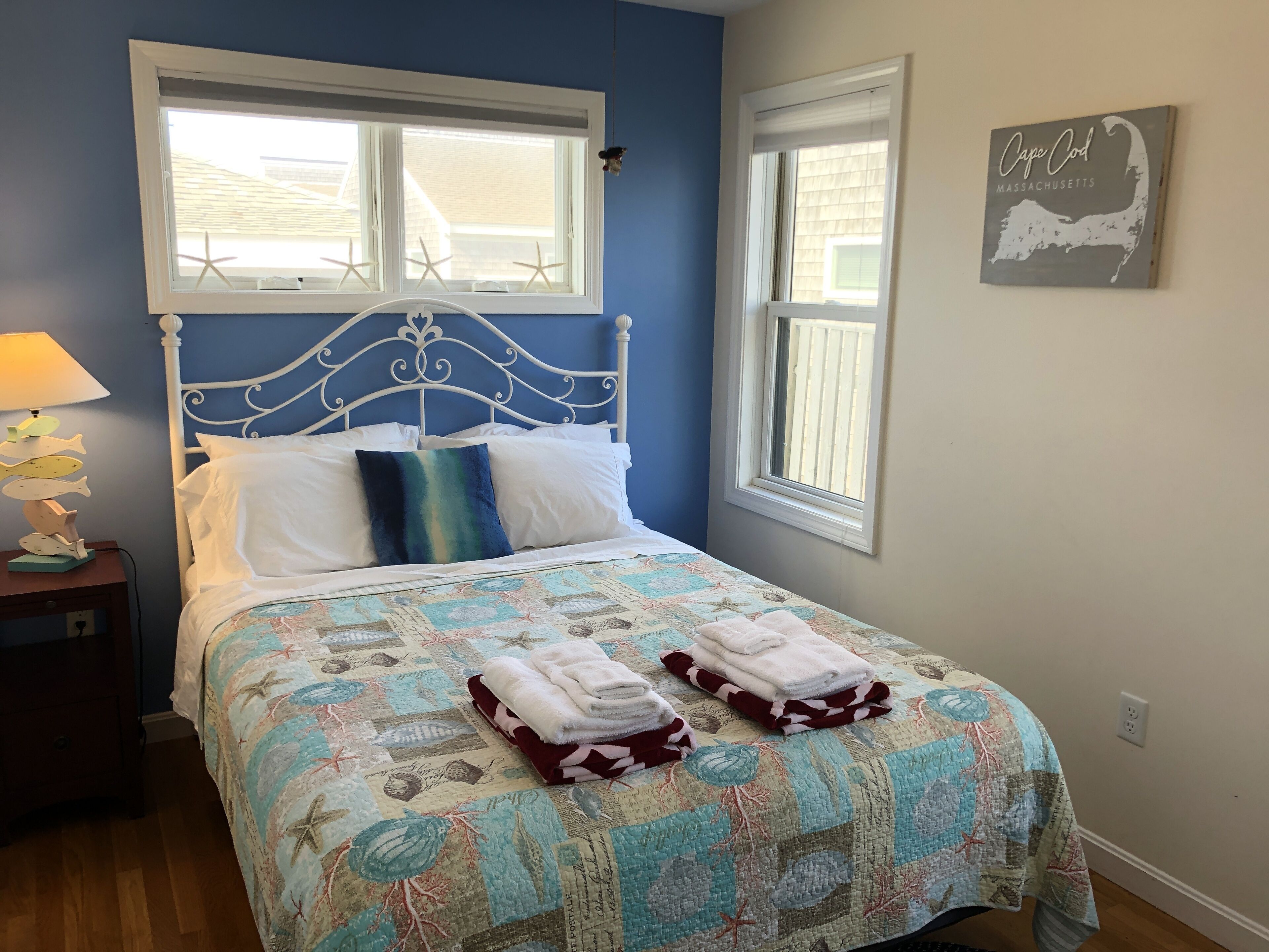 A bedroom with a bed, two windows, a wall clock, and a framed map.