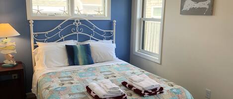 A bedroom with a bed, two windows, a wall clock, and a framed map.