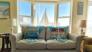 A corner seating area with a view of a sailboat, a framed picture, and a sign on the wall. - Lovely Oceanview 2 Bed 2 Bath with sleeper sofa, outdoor shower & rooftop deck! (North Truro)