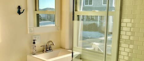 A bathroom with a glass-enclosed shower, a white sink, and a mirror above it.