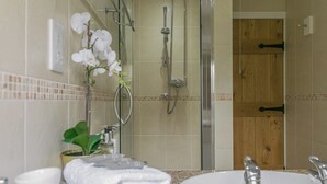 A bathroom with a sink, mirror, and shower. There are towels stacked on the counter and a potted plant. - 1 bedroom accommodation in Llangennith, near Swansea (Llangennith, near Swansea)