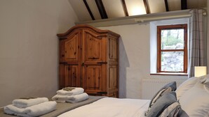 A bedroom with a bed, a wooden wardrobe, a window with a view of rocks, and a radiator. - 1 bedroom accommodation in Llangennith, near Swansea (Llangennith, near Swansea)