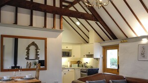 A spacious living area with a wooden dining table, a leather sofa, and a kitchen in the background. - 1 bedroom accommodation in Llangennith, near Swansea (Llangennith, near Swansea)