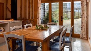 A dining area with a wooden table and chairs, a view of the garden through glass doors, and a rustic interior with exposed beams. - 3 bedroom accommodation in Ashdon, near Saffron Walden (Ashdon, near Saffron Walden)