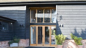 A building with a large glass door and windows, a brick foundation, and two potted plants. - 3 bedroom accommodation in Ashdon, near Saffron Walden (Ashdon, near Saffron Walden)