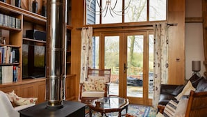 A cozy living room with a wood-burning stove, a bookshelf, a comfortable sofa, and a dining table. - 3 bedroom accommodation in Ashdon, near Saffron Walden (Ashdon, near Saffron Walden)