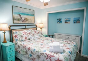 Ein Schlafzimmer mit einem Bett, zwei Nachttischlampen, einem Nachttisch, einer Kommode und einem Deckenventilator.