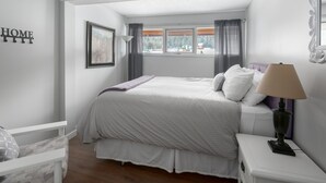 A bedroom with a large bed, a bedside table with a lamp, a framed picture on the wall, and a window with curtains. - Panorama Horsethief Lodge 2 bedroom condo, Sleeps 6: Unit 516 (Panorama)