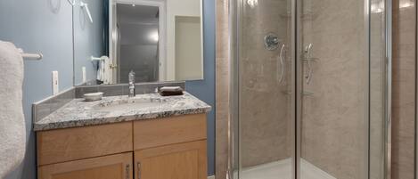 A bathroom with a glass-enclosed shower, a marble countertop, and wooden cabinets.