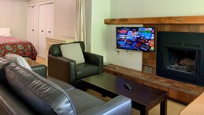 Un salon avec une cheminée, un téléviseur fixé au mur, un canapé, un fauteuil et une table basse.