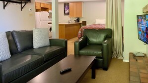 Un salon comprenant un canapé, une table basse, un fauteuil en cuir et un téléviseur fixé au mur.