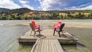 A wooden dock with two red chairs facing a lake, surrounded by hills and trees. - Rayleigh Riverfront Retreat -BEAUTIFUL GARDEN OASIS (Kamloops)
