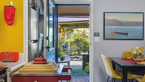 A dining area with a table, chairs, and a view of a garden through an open door. - Rayleigh Riverfront Retreat -BEAUTIFUL GARDEN OASIS (Kamloops)
