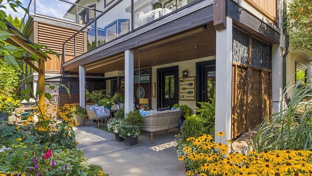 A modern house with a covered porch, outdoor seating, and a garden with yellow flowers. - Rayleigh Riverfront Retreat -BEAUTIFUL GARDEN OASIS (Kamloops)