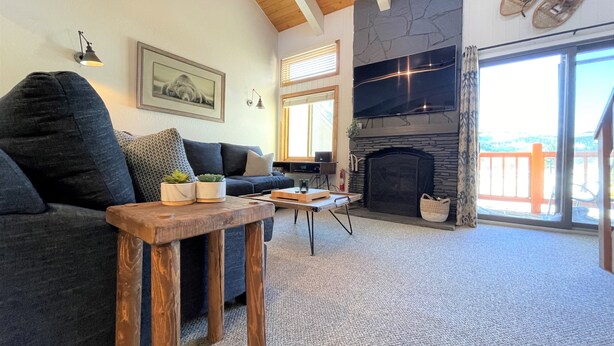 Ein gemütliches Wohnzimmer mit einem dunkelgrauen Sofa, einem Holztisch, einem Kamin und einem großen Fernsehbildschirm.