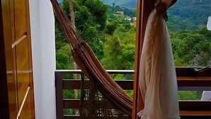 Un hamac sur un balcon, avec vue sur un paysage verdoyant et luxuriant et sur des bâtiments situés au loin.