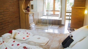 Une chambre comprenant un lit, une douche en verre, un banc en bois et une petite table avec des articles de toilette.