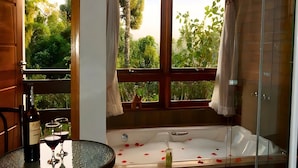 Une salle de bain avec une baignoire, une table ronde avec une bouteille et des verres, et une fenêtre avec des rideaux.