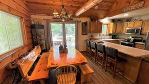 A wooden cabin interior with a dining area, kitchen, and a view of the outdoors.