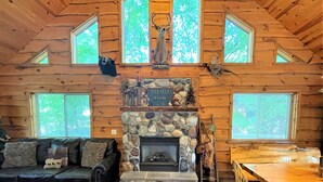 A log cabin interior with a stone fireplace, a black leather sofa, a dining table, and a birdcage.