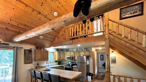 A rustic kitchen with wooden beams, a central island with bar stools, a stainless steel refrigerator, and a wooden staircase.